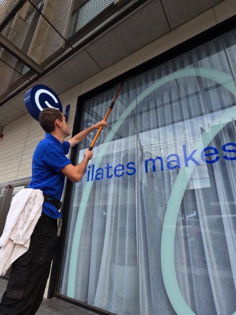 Commercial window cleaner cleaning a store front window using a extended pole.
