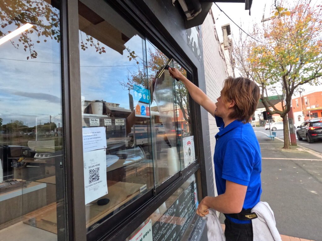 Commercial window cleaner cleaning a cafe shop front window with a squeegee.
